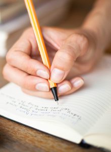 Photo of a hand with a pen making notes in a notebook